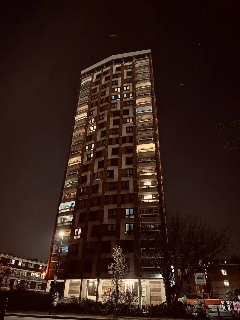 A council tower block at night, lit windows scattered up its face.