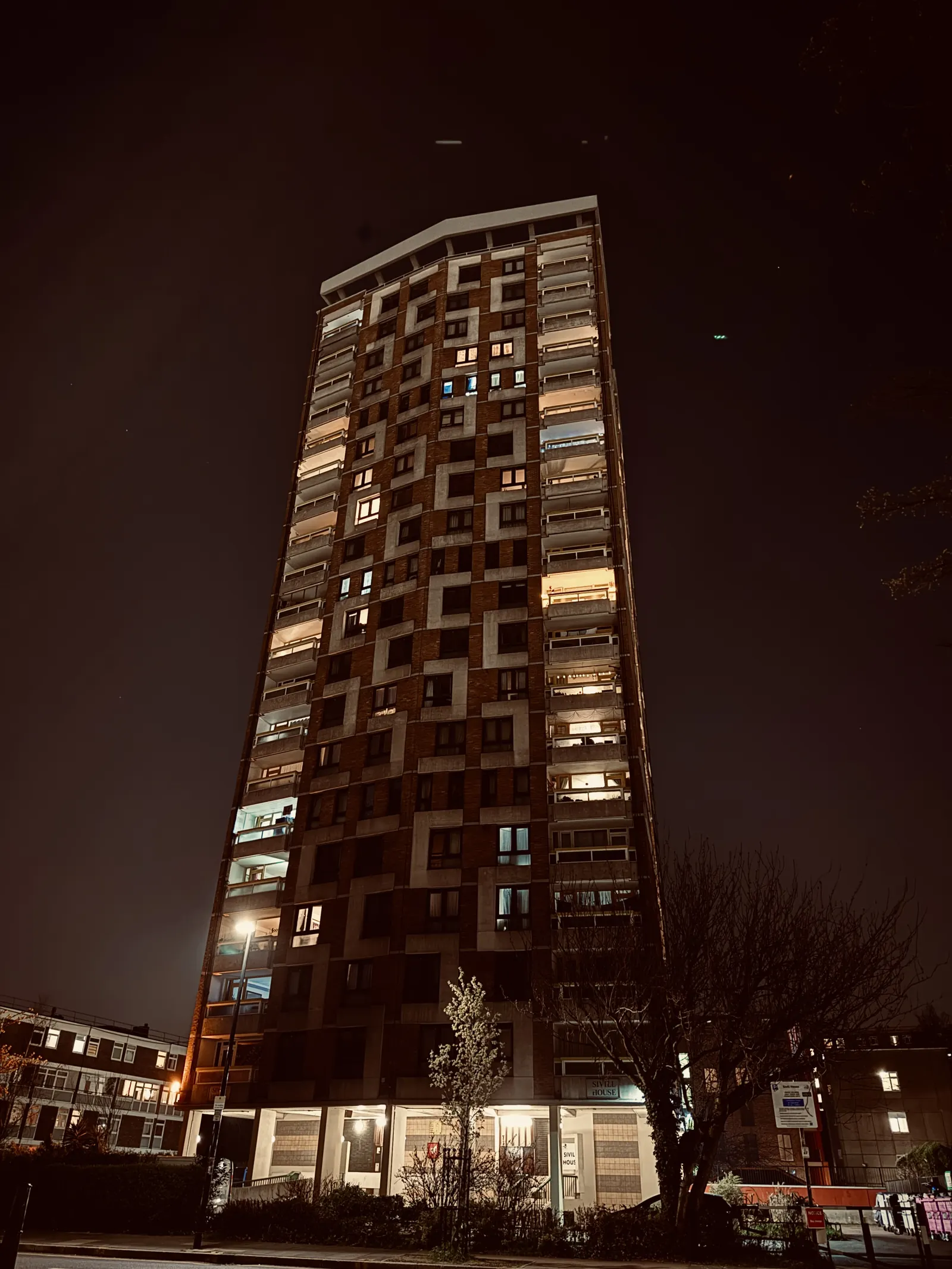 A council tower block at night, lit windows scattered up its face.